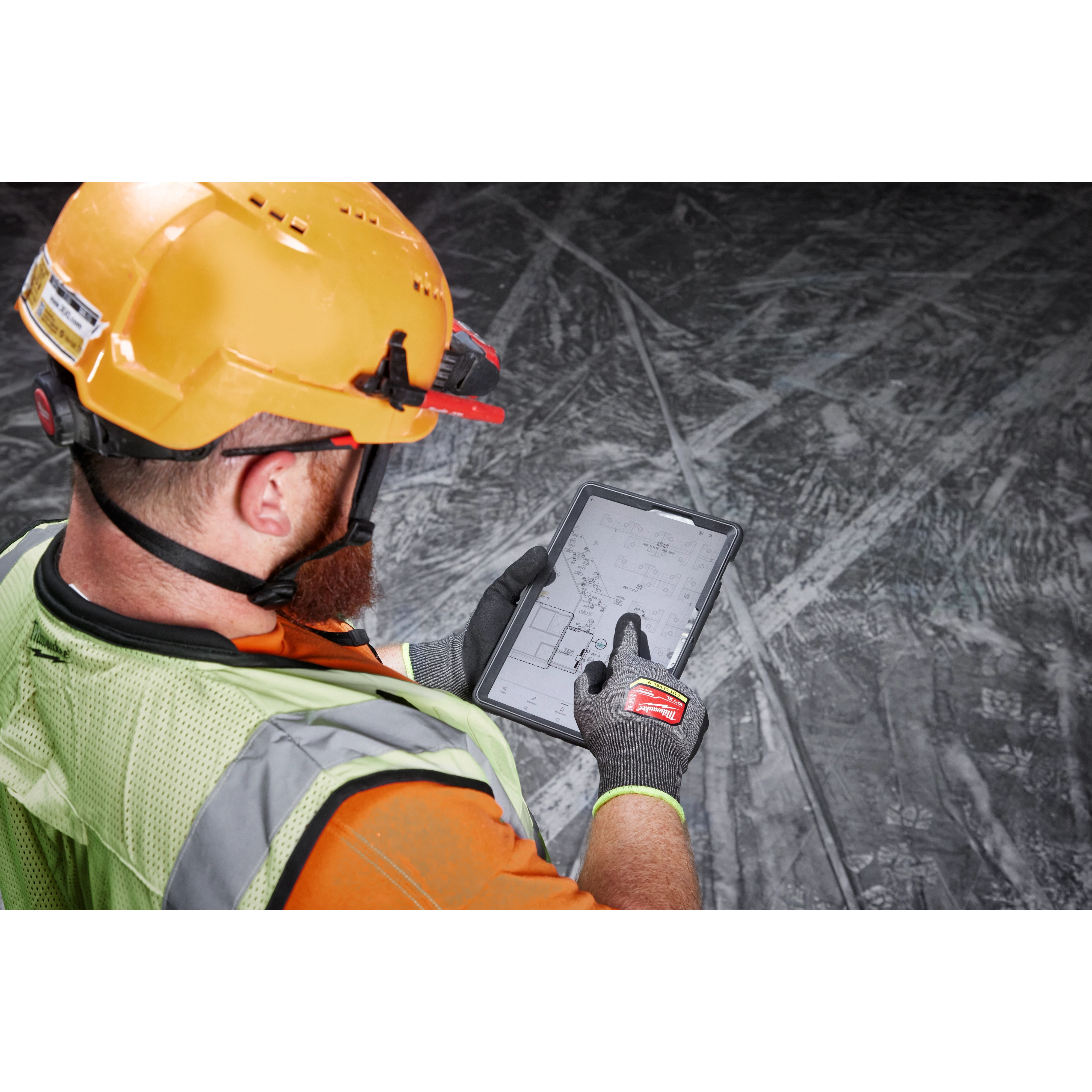 Worker in a yellow hard hat and vest uses a tablet while wearing Cut Level 9 High-Dexterity Nitrile Dipped Gloves - L.