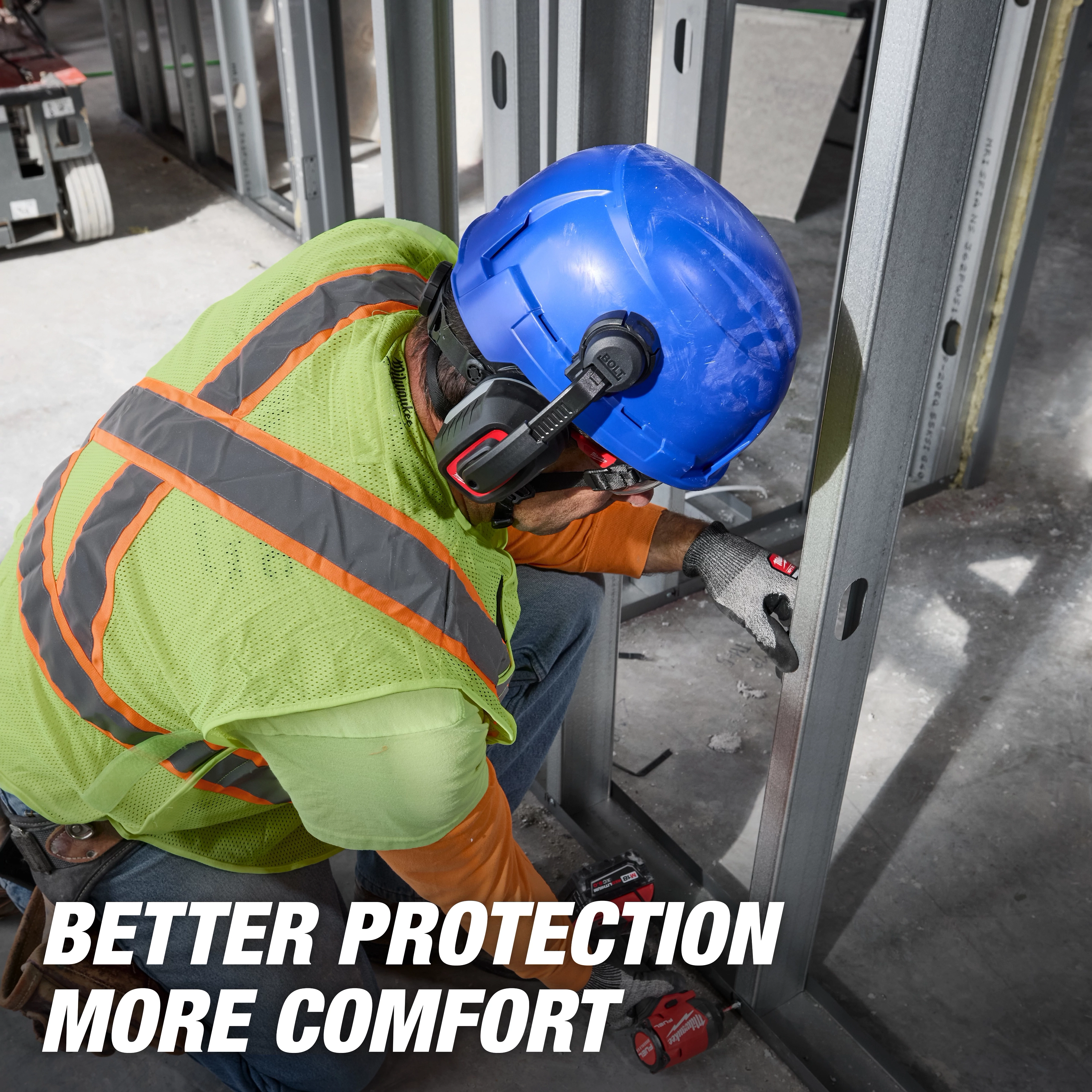 Worker wearing a blue BOLT 4PT Full Brim Vented Safety Helmet - Type 2, Class C, and neon safety vest, using a drill on metal framing.
