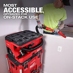 Worker using M18 FUEL 4 Gallon Wet/Dry Vacuum w/ PACKOUT Compatibility & VACLINK on stacked tool boxes near a wall.