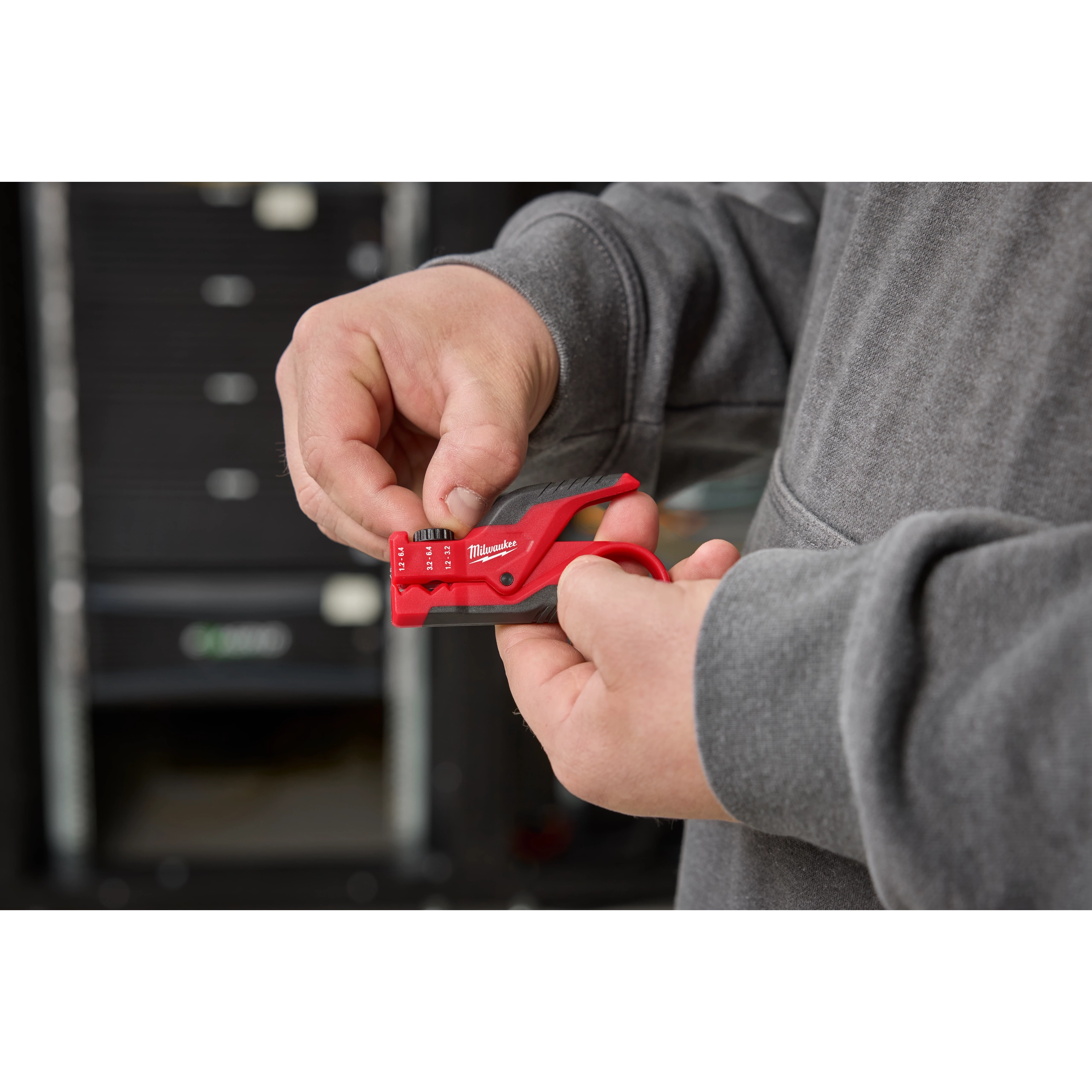 A person uses a red Buffer Tube Ringer & Slitter tool to strip cables. They are holding the tool in both hands, with a gray jacket visible.