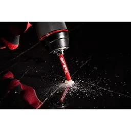 A Milwaukee® 1/4" DIAMOND MAX™ Hole Saw Bit is attached to a power drill, cutting through a dark material. Dust and debris can be seen around the drilling site. The bit is red with white text and branding.