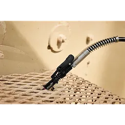 M18 FUEL Grease Gun nozzle and hose positioned on a metal grid surface.