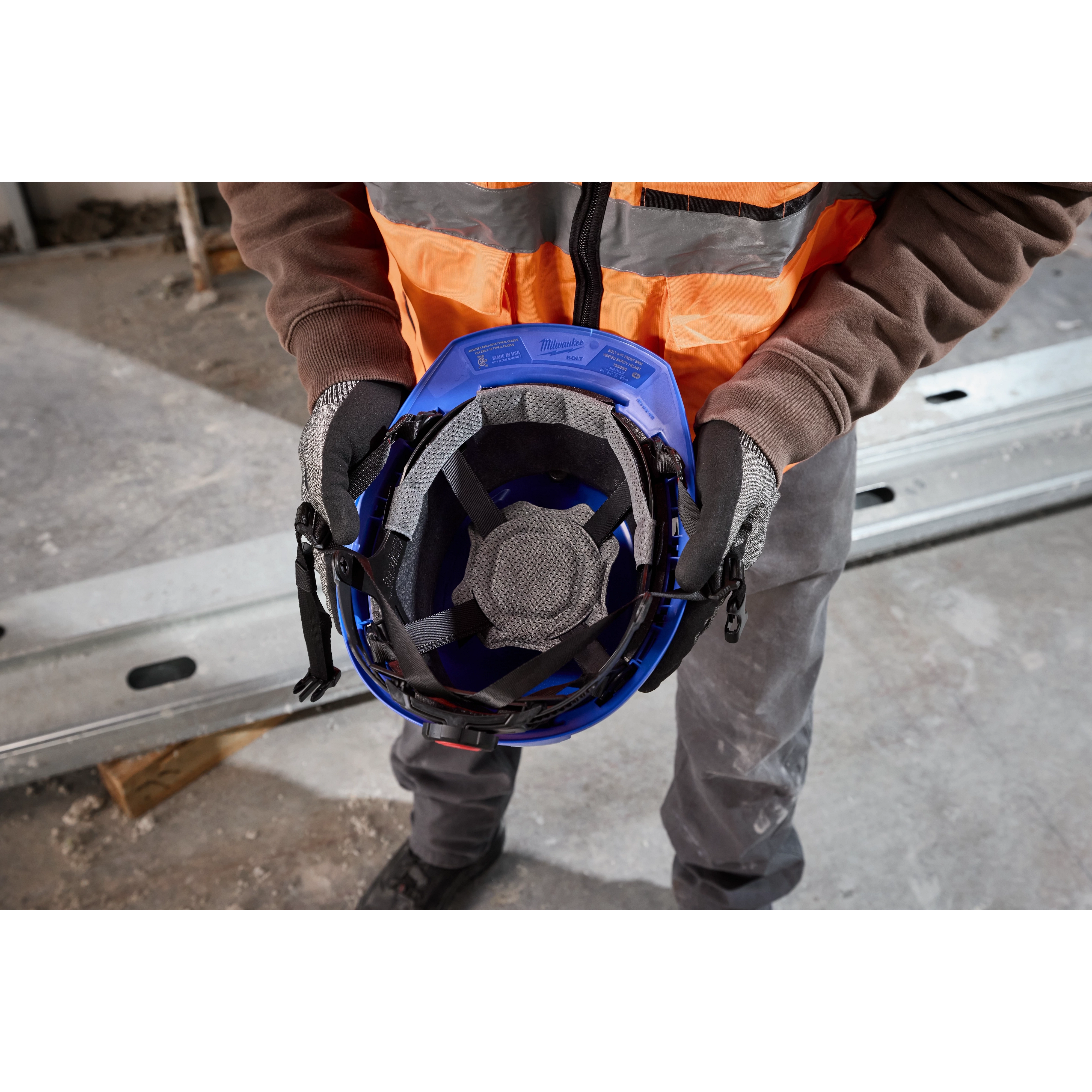 Worker holds BOLT 4PT Blue Front Brim Non-Vented Safety Helmet – Type 2, Class E, showing the interior suspension system and padding.