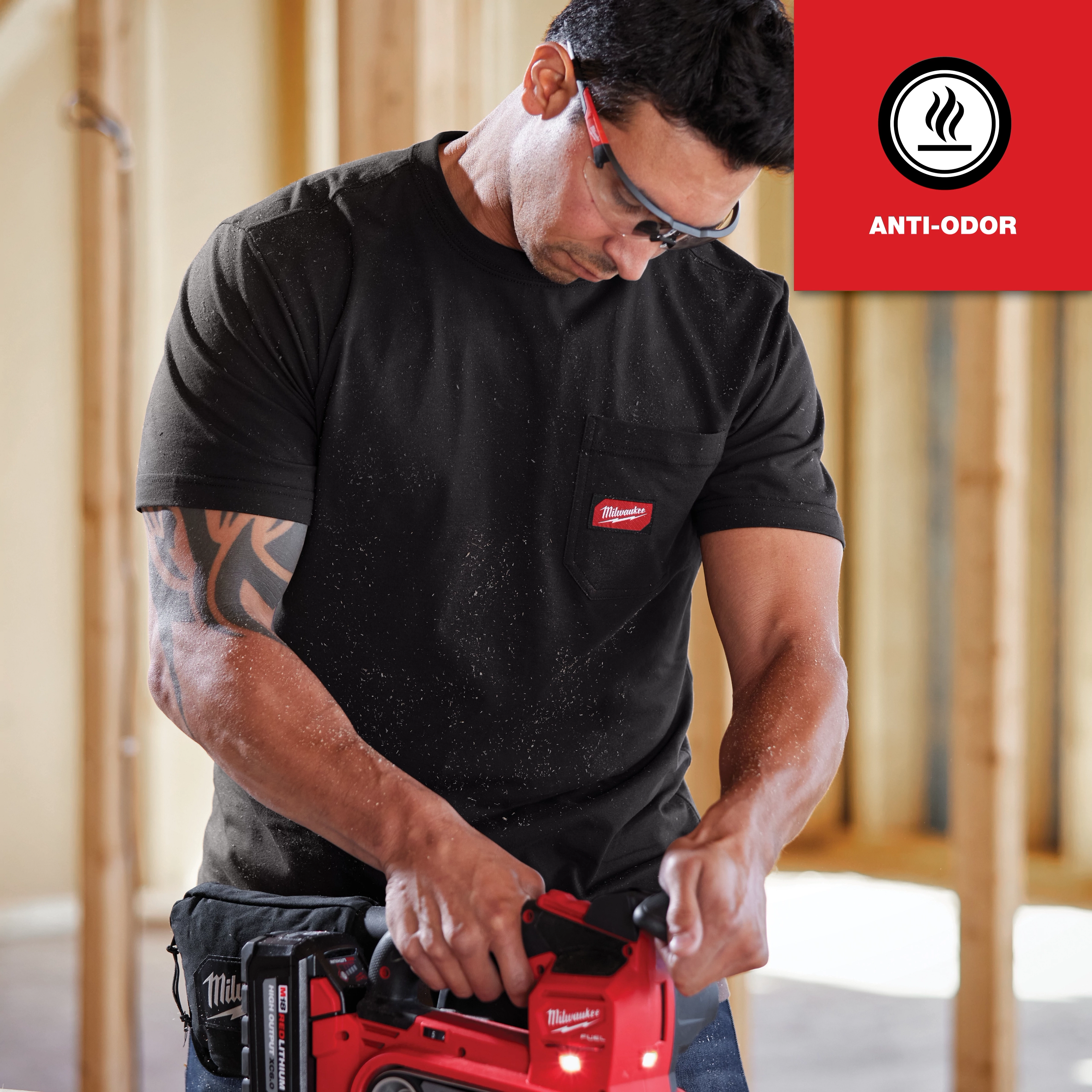 Man wearing a black GRIDIRON Pocket T-Shirt - Short Sleeve Anti-odor while operating a red power tool in a construction setting.