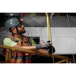 A construction worker wearing a hardhat and safety vest uses a measuring tape while wearing Cut Level 6 High-Dexterity Nitrile Dipped Gloves - L.