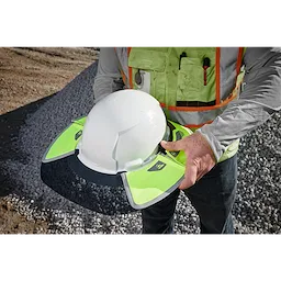 A person is holding a hard hat fitted with a BOLT Sun Visor. The sun visor is neon green with reflective elements and designed to attach to a standard hard hat for added shade and visibility.
