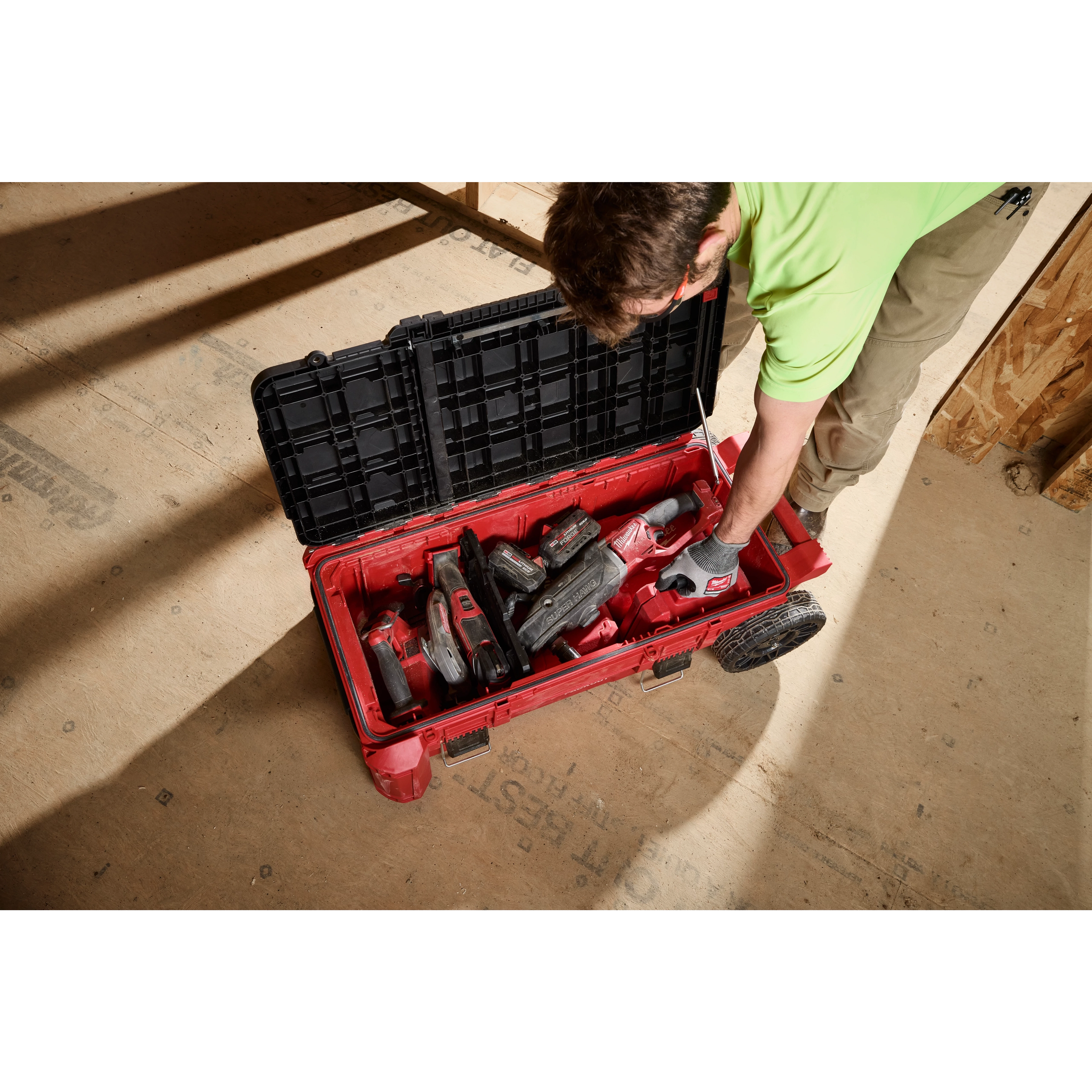 Worker reaching into PACKOUT Compact Rolling Tool Chest filled with power tools on a construction floor.