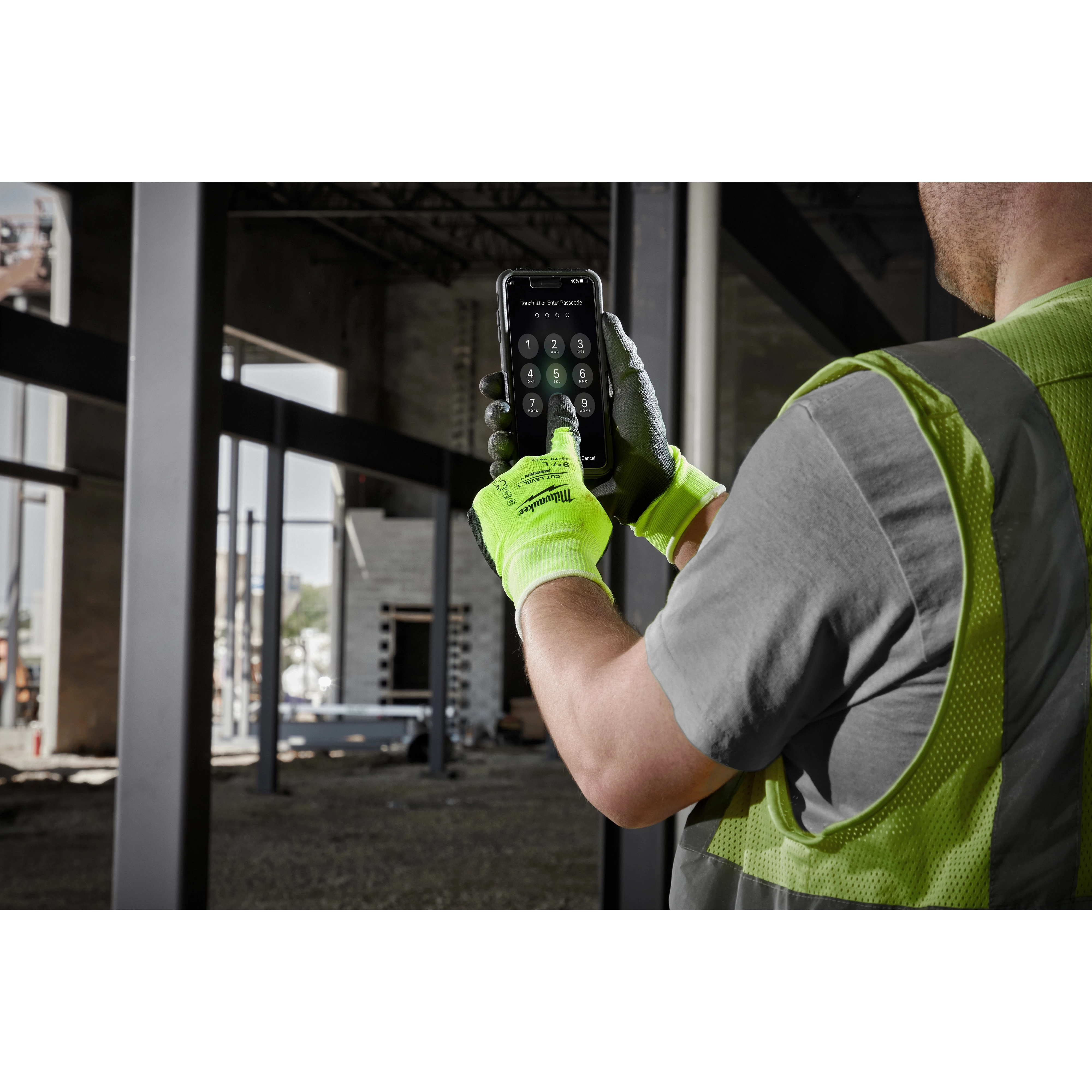Person wearing High Visibility Cut Level 1 Polyurethane Dipped Glove - L, operating a smartphone on a construction site.