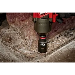 SHOCKWAVE Impact Duty™ 1/2" Drive 1-3/16" Deep 6 Point Socket, attached to a power tool, is being used by a gloved hand to work on a metal structure. The socket is black with white text indicating size, and the surrounding area shows a worn industrial surface.