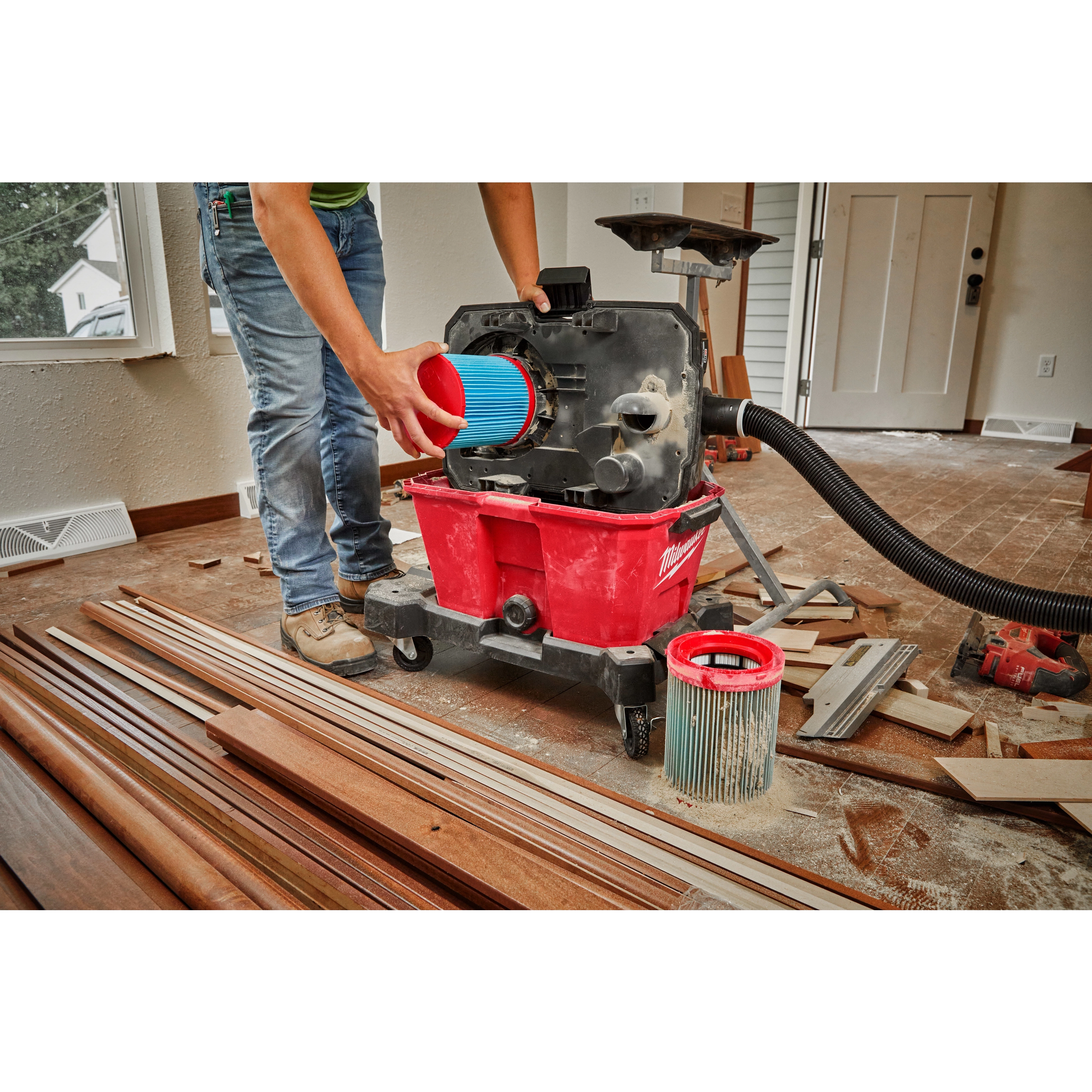 Person installing a blue MILWAUKEE Large Wet/Dry Vacuum High Efficiency Filter into a red vacuum unit on a construction site.