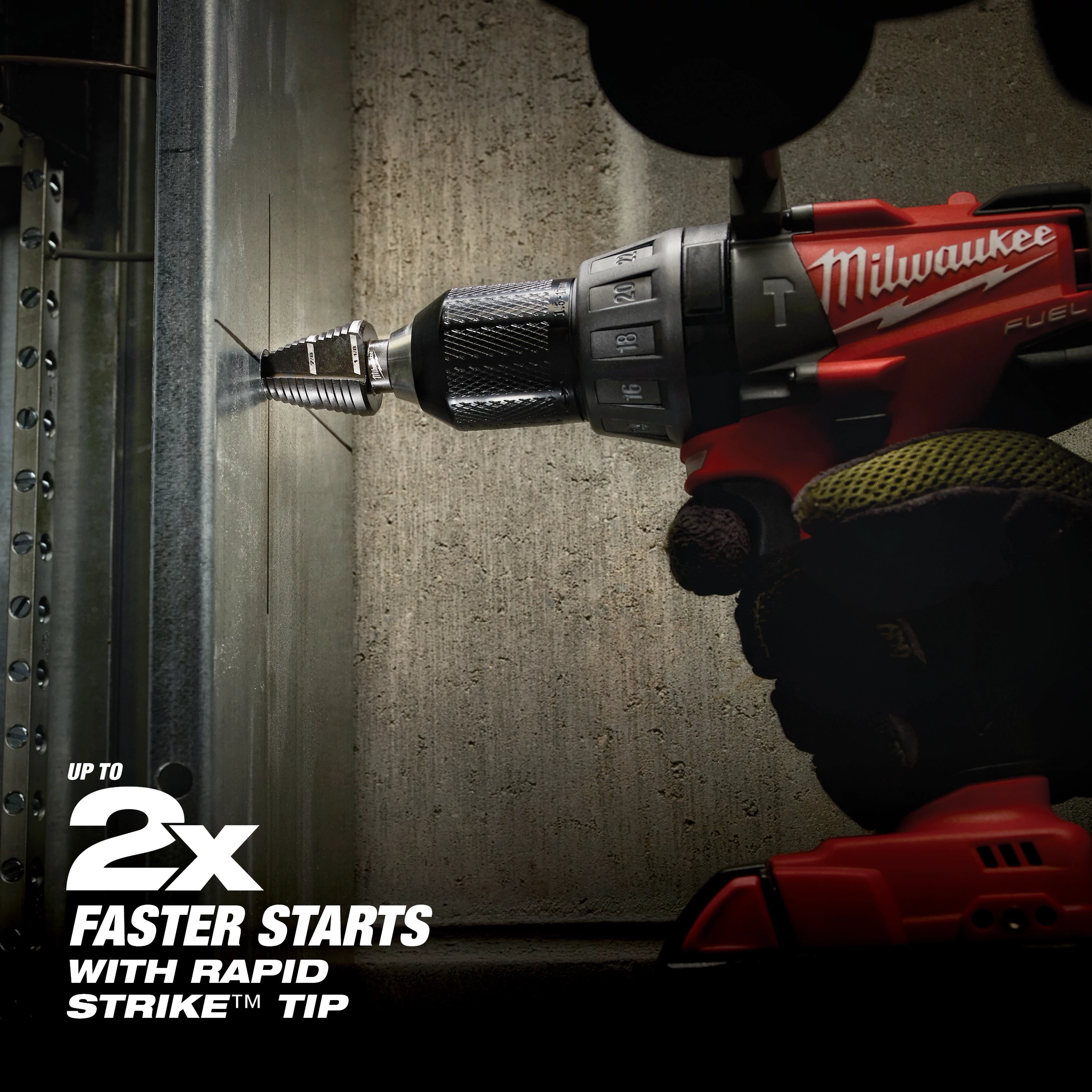 A red and black cordless drill is being used by a gloved hand to bore through a metal wall, showcasing Jam Free Step Bits. Text indicates the product offers "up to 2x faster starts with Rapid Strike tip." The drill and bits are positioned horizontally against the wall during operation.