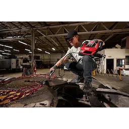 Worker using an M18 FUEL Grease Gun to apply grease on large industrial machinery.