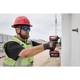 A construction worker in a red hard hat and fluorescent safety vest uses a battery-operated impact driver to secure a bolt. The worker is wearing Polarized Full Frame Safety Glasses with Removable Side Shields – Blue Mirrored Dual Coat Lenses, providing robust eye protection in an outdoor work environment.