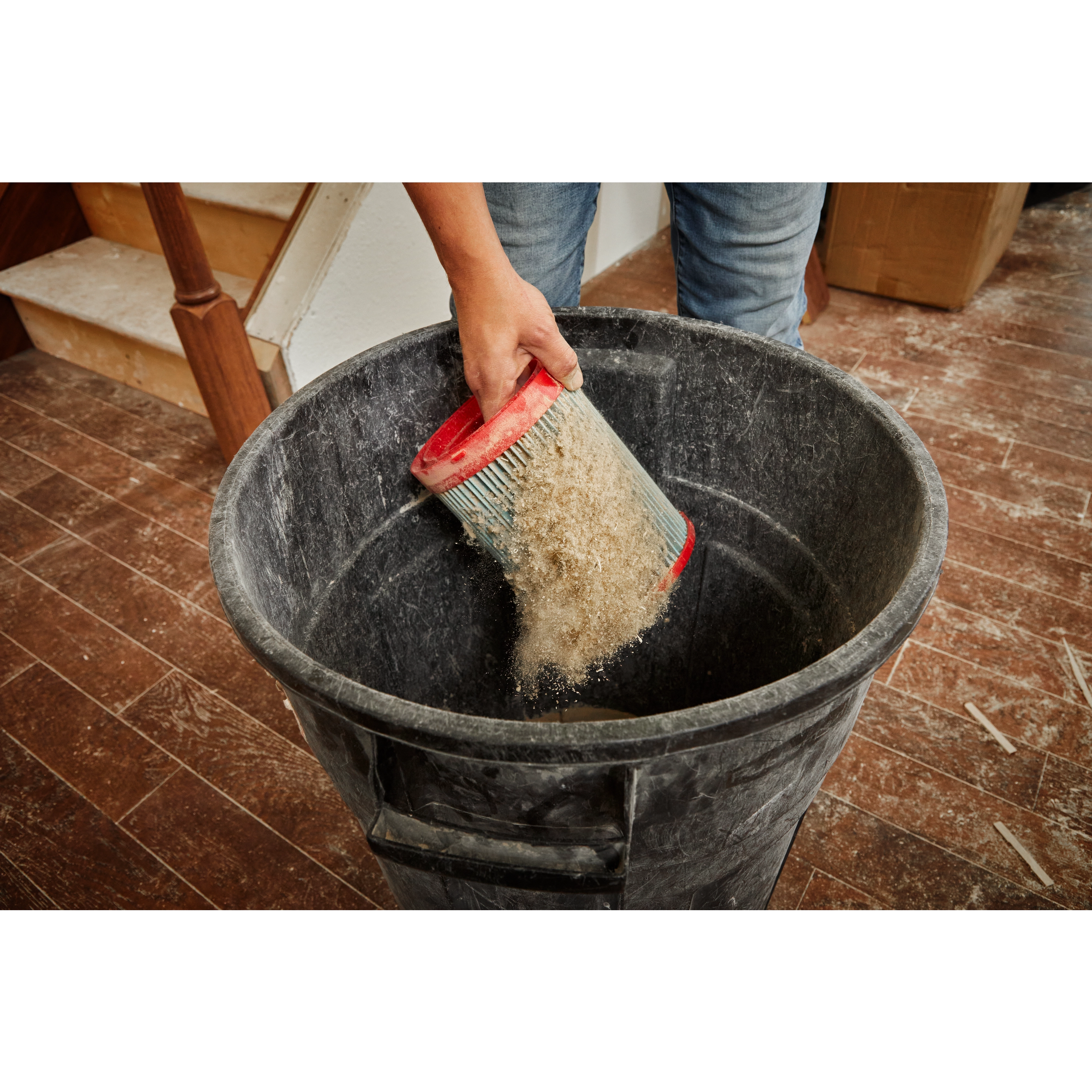 Person emptying the MILWAUKEE Large Wet/Dry Vacuum High Efficiency Filter filled with dust into a black trash bin.