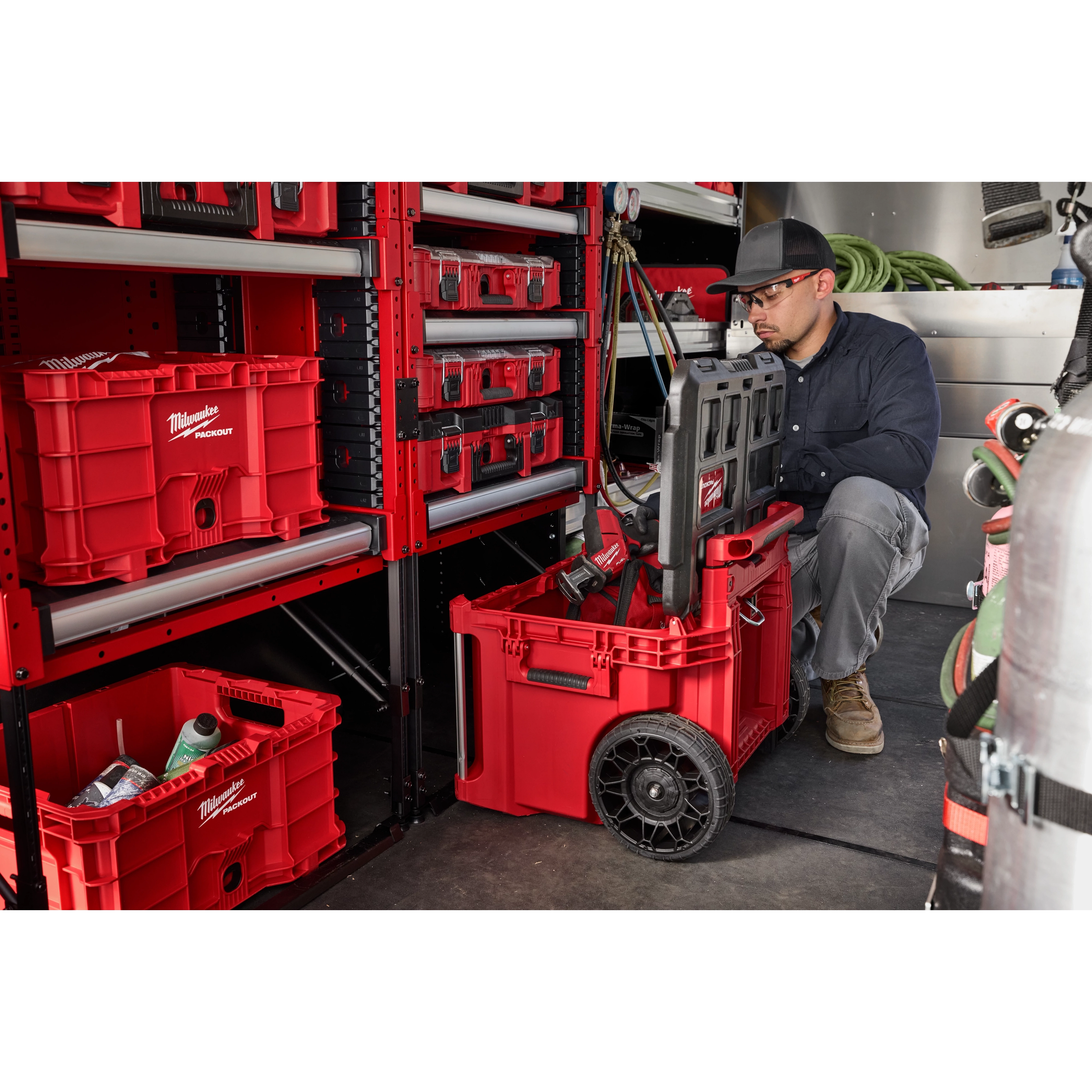 Milwaukee Packout storage system includes various red modular toolboxes on shelves and a wheeled toolbox on the floor. The toolboxes have secured compartments and are designed for arranging and transporting tools efficiently.