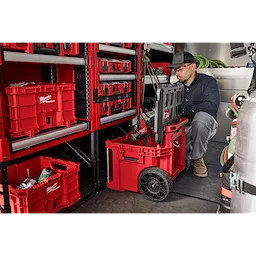 Milwaukee Packout storage system includes various red modular toolboxes on shelves and a wheeled toolbox on the floor. The toolboxes have secured compartments and are designed for arranging and transporting tools efficiently.