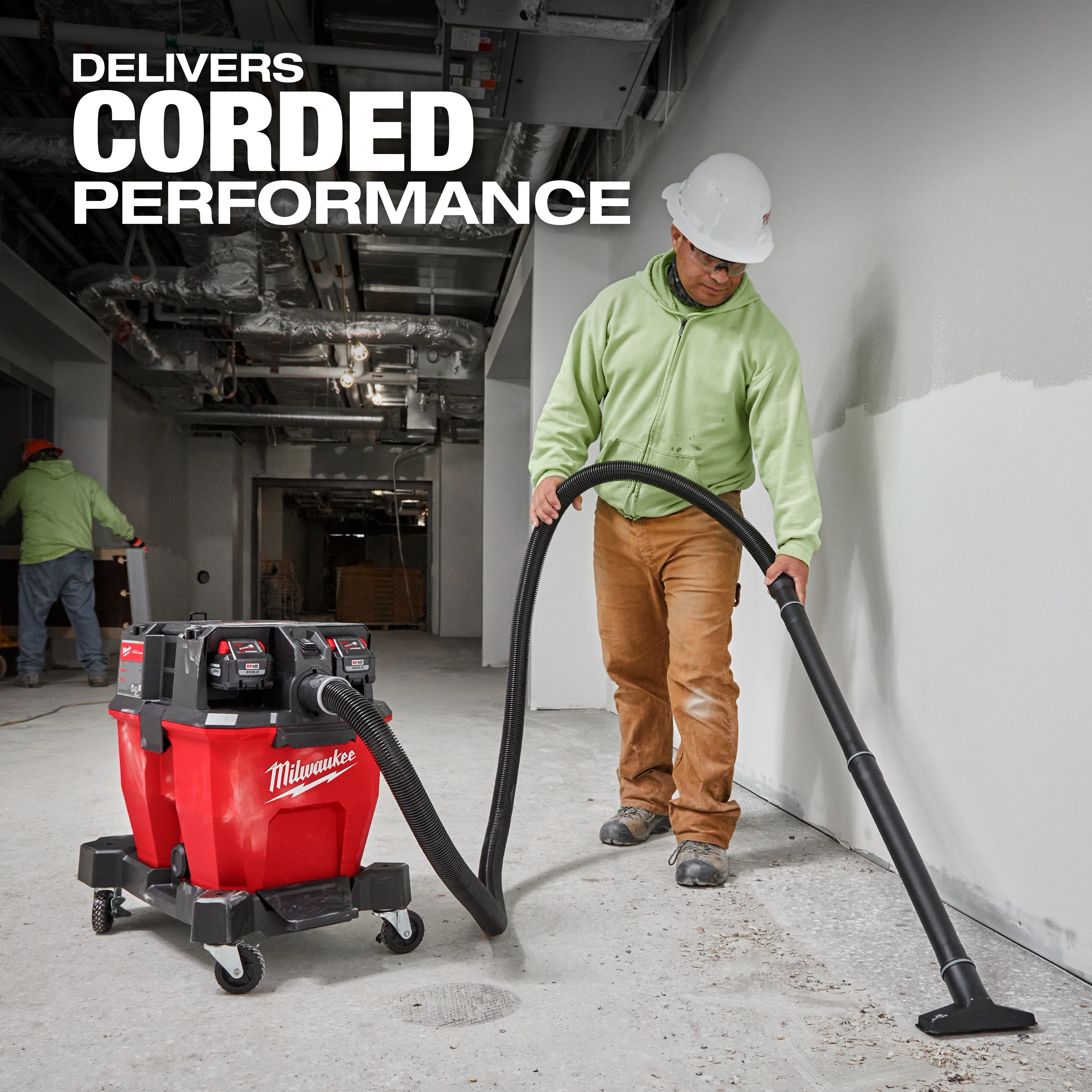 The M18 FUEL™ NEXUS™ 9 Gallon Dual-Battery Wet/Dry Vacuum is being used by a construction worker in a building under construction. The vacuum is red and black, labeled with "Delivers Corded Performance," and is designed for heavy-duty cleaning tasks.