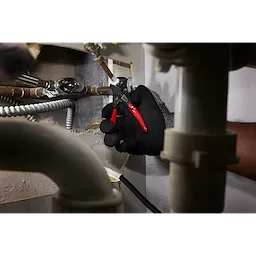 A hand wearing a black glove uses the 5" Pliers Wrench W/ Belt Clip to tighten a metal pipe connection in a tight space, surrounded by various plumbing and electrical components.