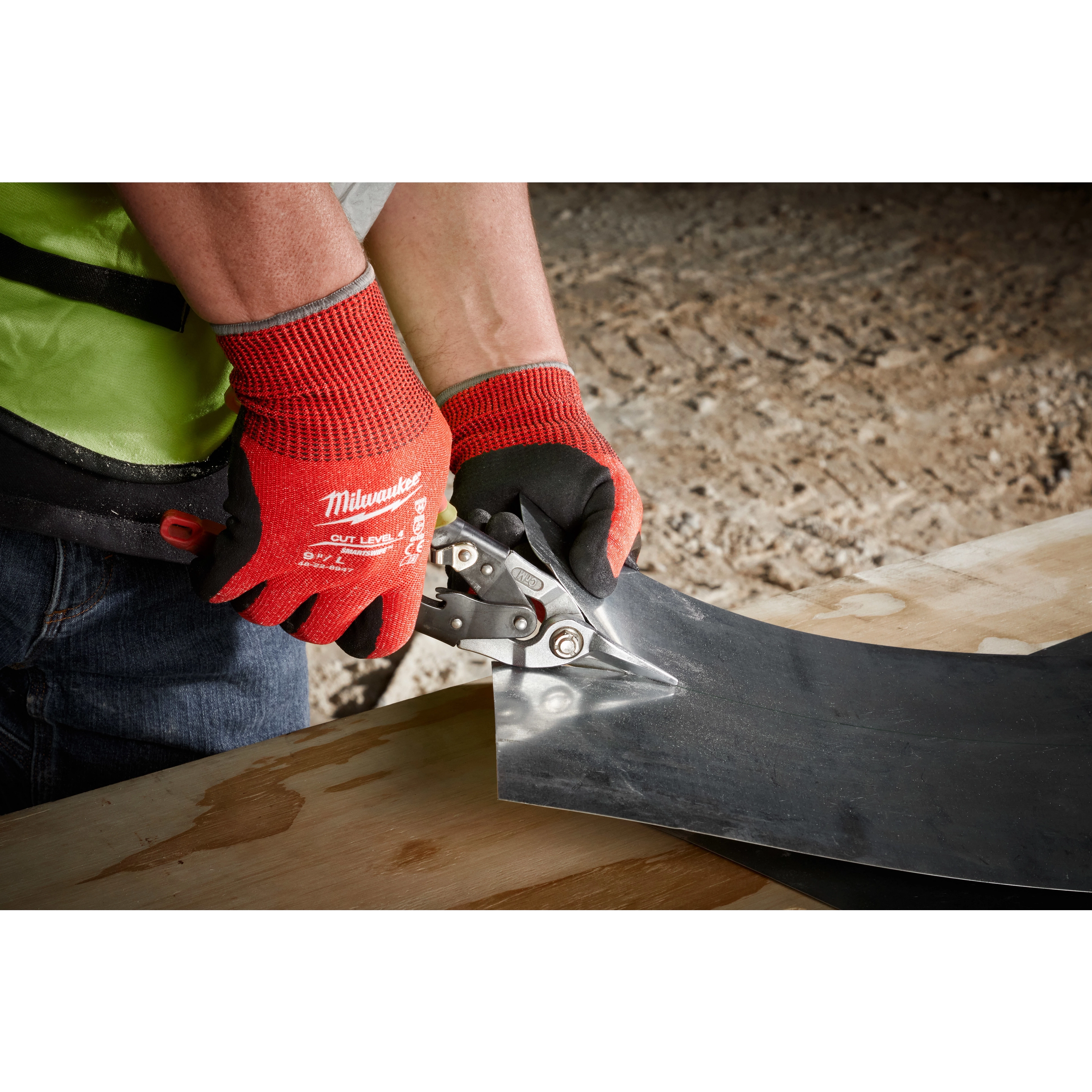 Person wearing Cut Level 4 Nitrile Dipped Glove - L uses metal snips to cut through a sheet of metal on a wooden surface.