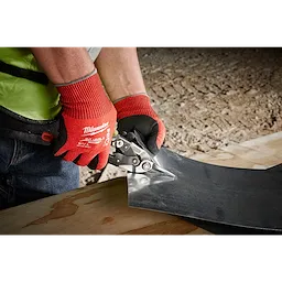 Person wearing Cut Level 4 Nitrile Dipped Glove - L uses metal snips to cut through a sheet of metal on a wooden surface.