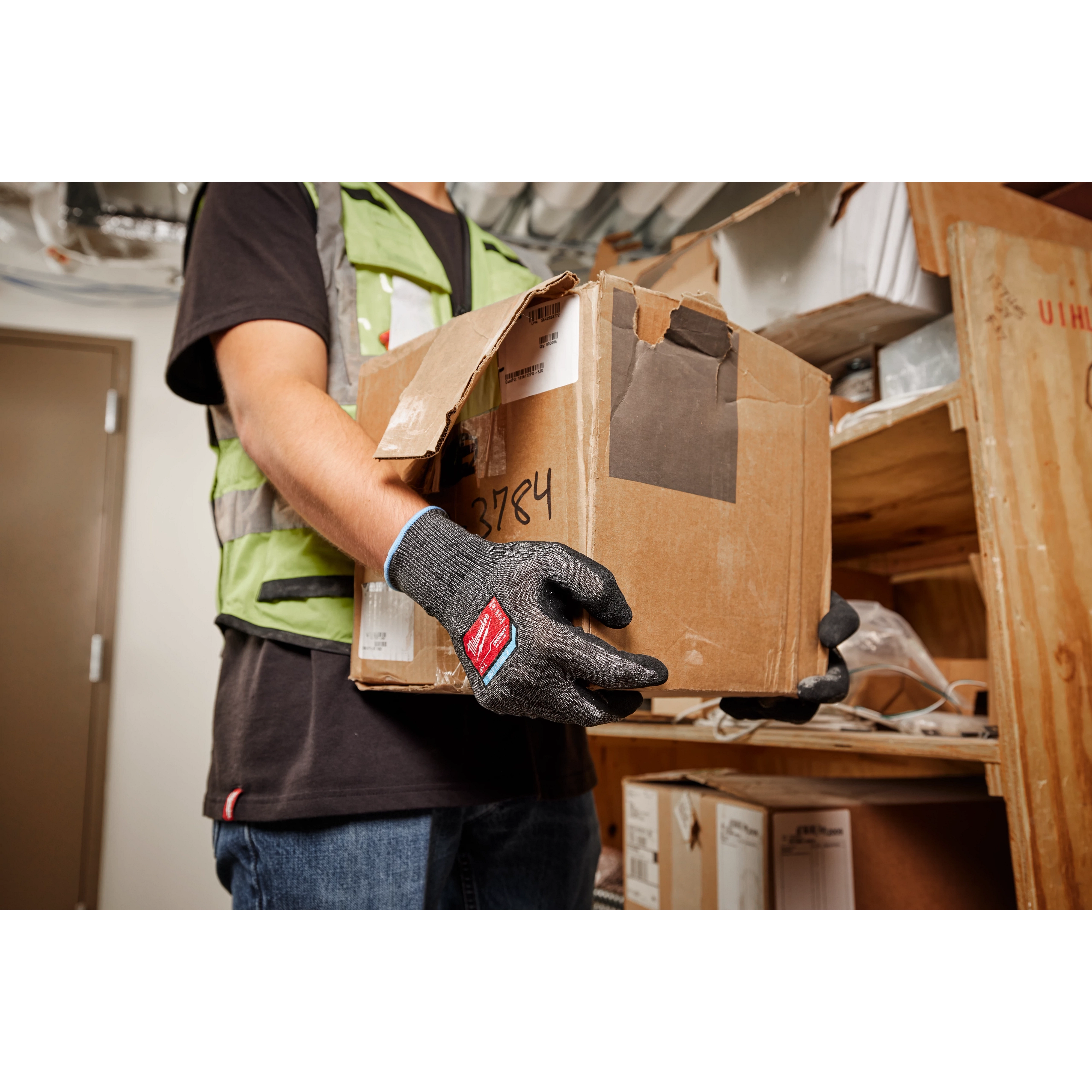 Person wearing Cut Level 2 High-Dexterity Nitrile Dipped Gloves - L, lifting a cardboard box in a storage room.