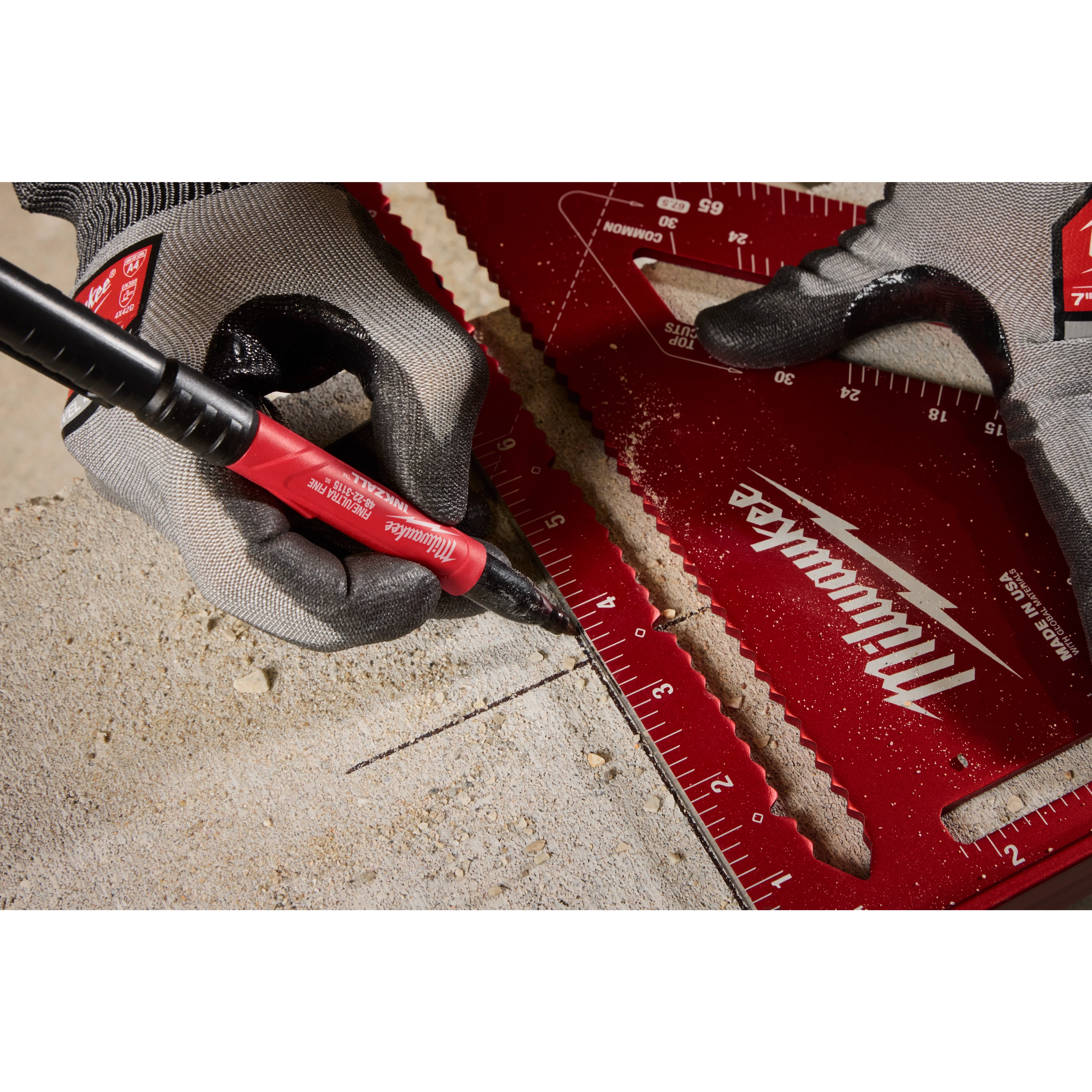 A gloved hand uses the INKZALL Double-Sided Black Jobsite Marker—Ultra Fine & Fine Point to draw a line on a piece of concrete. The marker is held against a ruler.